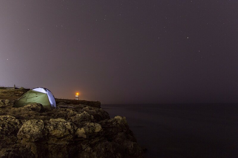Палатка и маяк на скалистом берегу Чёрного моря ночью среди звёзд (Севастополь, Крым)