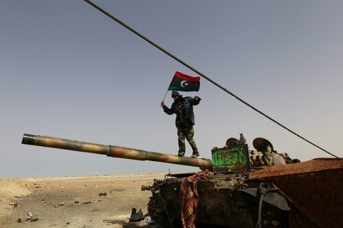 A rebel fighter walks on a tank along the road between Ajdabiyah and Brega
