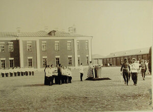 Император Николай II (справа) и сопровождающие его лица проходят по плацу во время молебна по случаю начала смотра артилерийских частей; в центре - священник и группа певчих