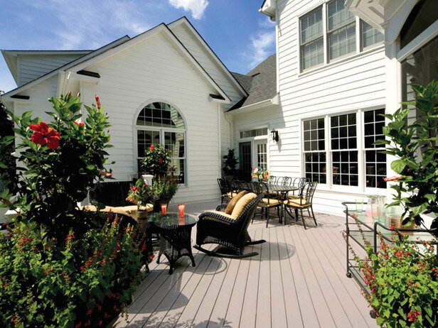 Composite deck with black wicker furniture, flowers and plants, white home exterior, and windows.