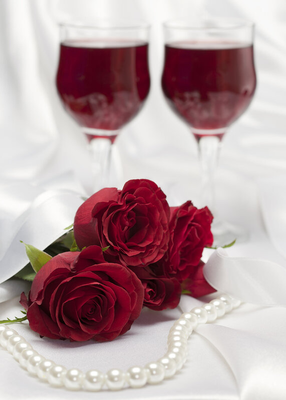 Red roses with a string of white pearls and glasses of red wine