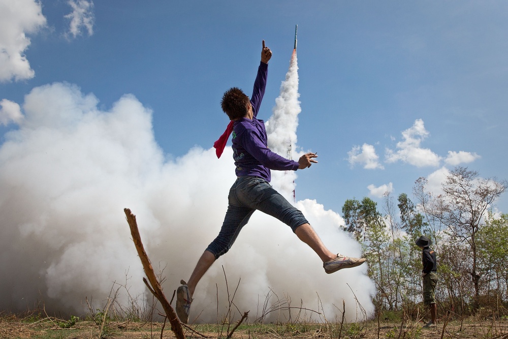 Молодой человек подпрыгивает в воздухе в знак радости на фестивале ракет Бунг Банг Фай, чтобы отпраз